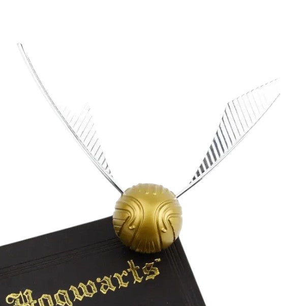 Golden Snitch replica from Harry Potter, displayed on a Hogwarts book, featuring intricate wings and gold detailing